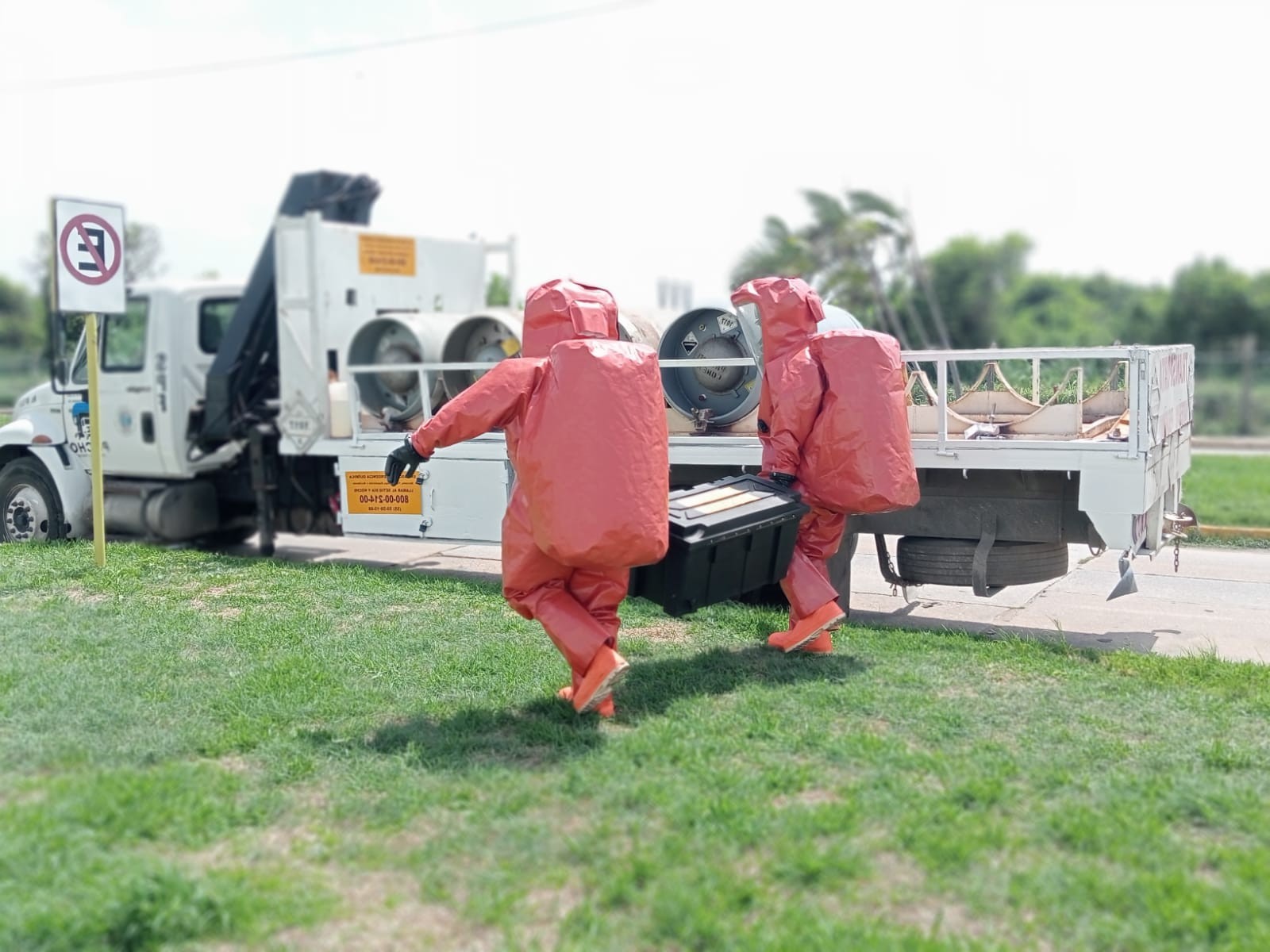 Personal con trajes de protección química transporta equipo junto a un vehículo